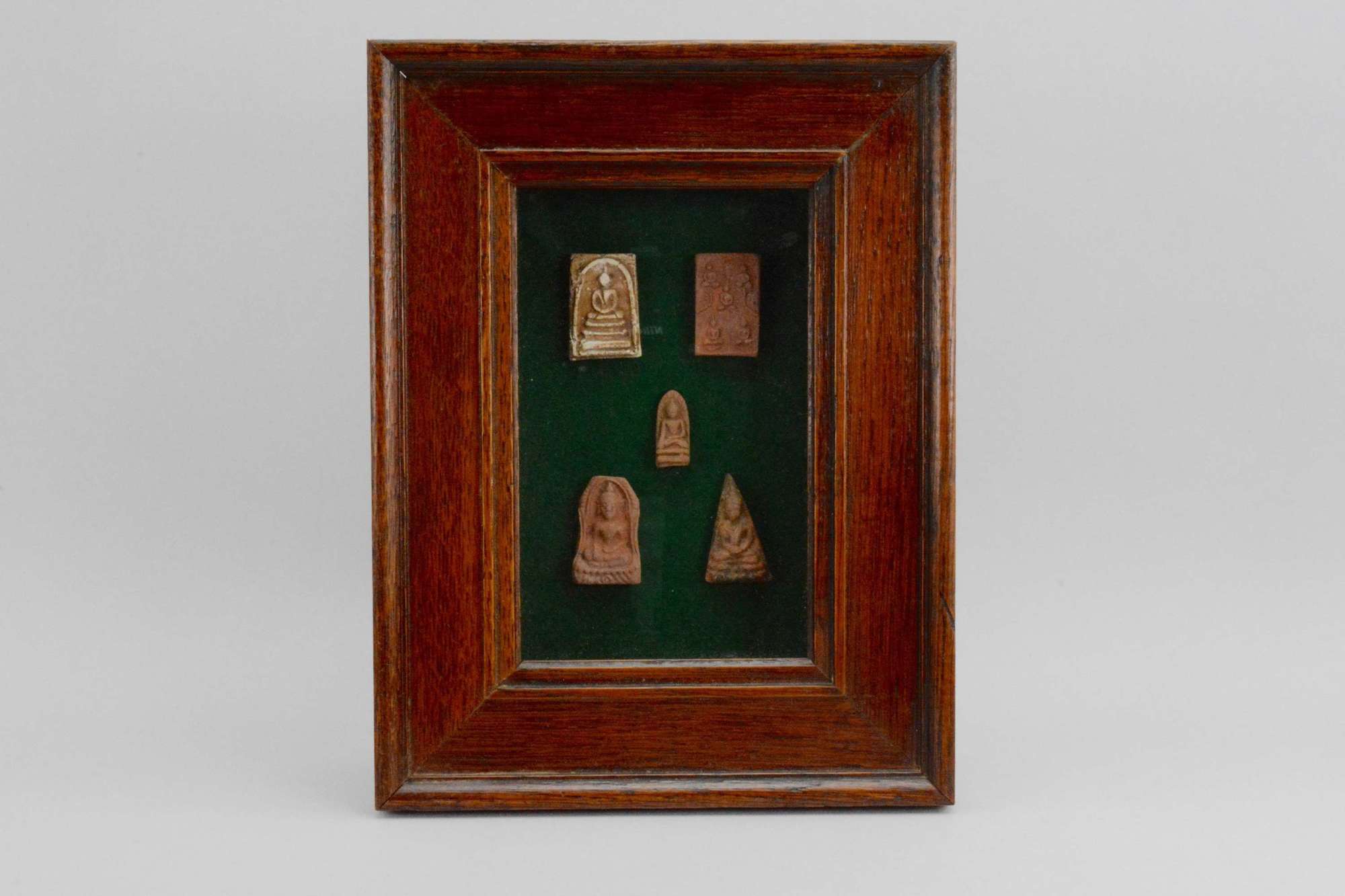 Five antique Thai pottery Buddha amulets mounted in an oak box frame