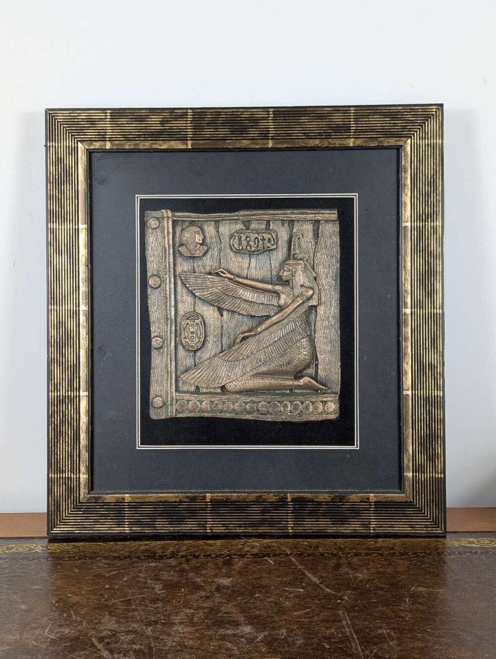 Framed Egyptian revival wall plaque of winged goddess kneeling in profile with cartouches