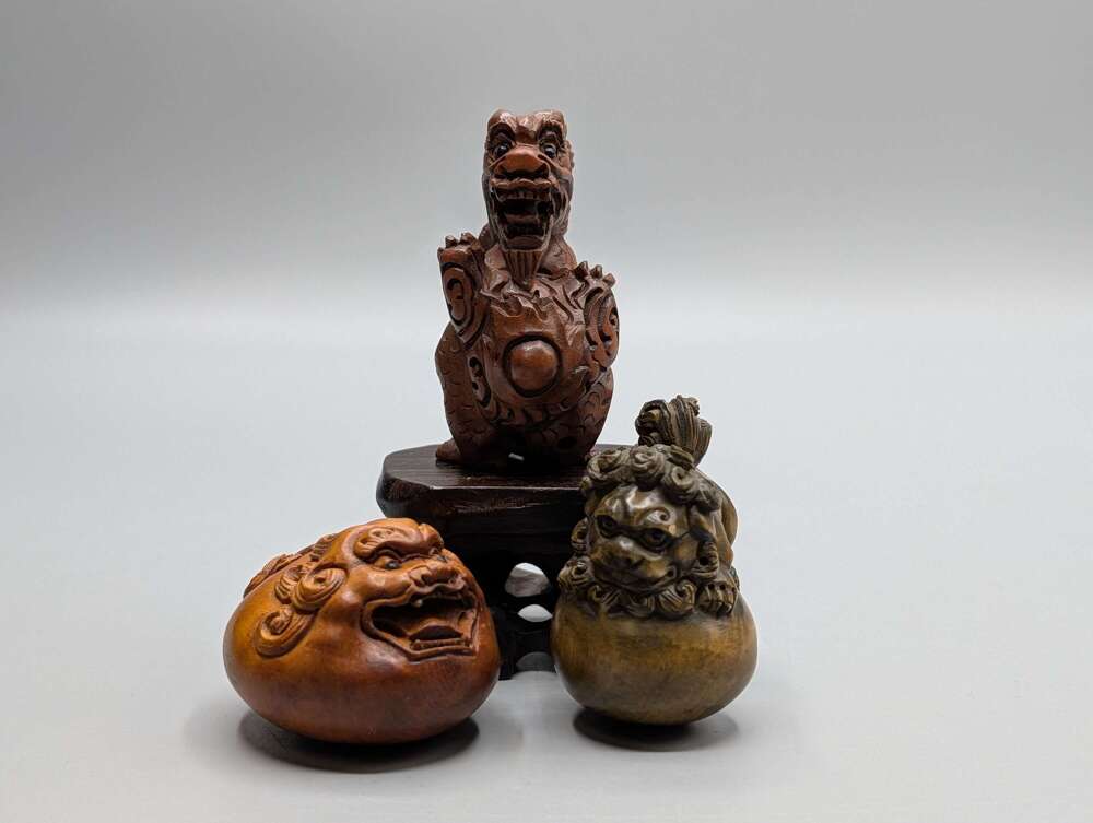 Japanese boxwood mythical beast netsukes, group of three signed with hardwood stand